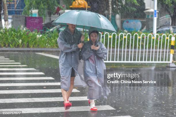 Pedestrians holding an umbrella walk along a road during a heavy rainfall as Typhoon Talim approaches on July 17, 2023 in Haikou, Hainan Province of...
