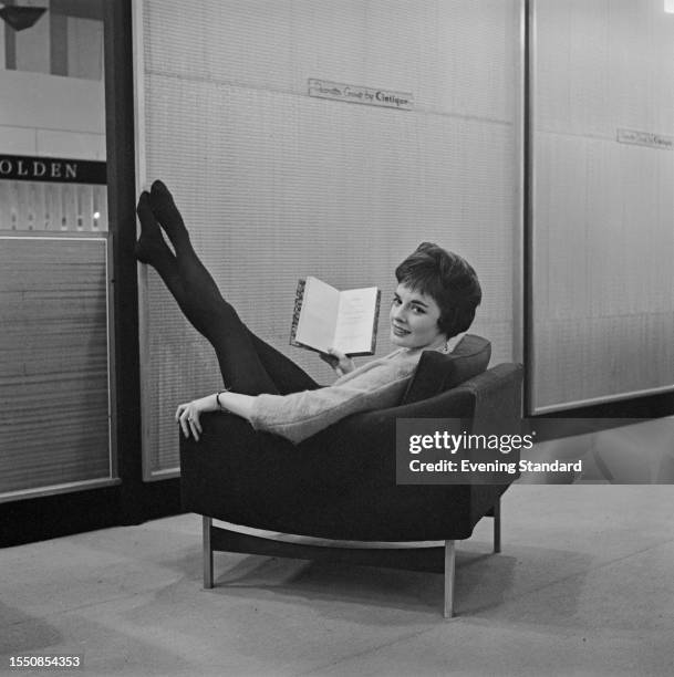 Woman seated in an armchair stretches her legs in the air at a furniture tradeshow in London, March 31st 1959.