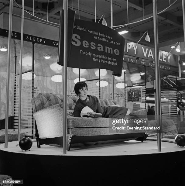 Model lying on a 'Sesame' sofa bed at a furniture tradeshow in London, March 31st 1959. A sign above reads 'For blissful comfort both ways as a...