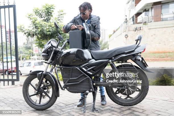 young african commuter putting smart battery into motorcycle - battery swapping electric vehicle technology stock pictures, royalty-free photos & images