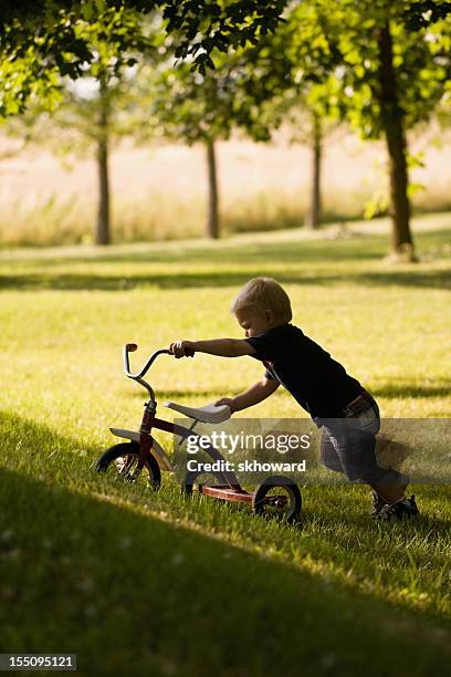 little boy pushing tricycle uphill - tricycle stock pictures, royalty-free photos & images