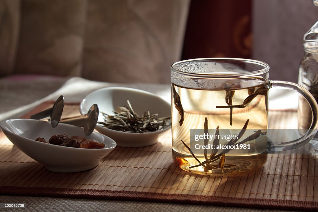 A glass cup with hemp tea and white bowls on a wooden table