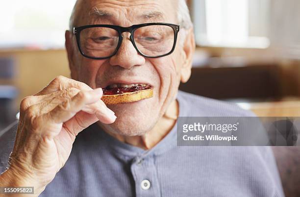 senior man eating toast and jelly jam - old man close up stockfoto's en -beelden