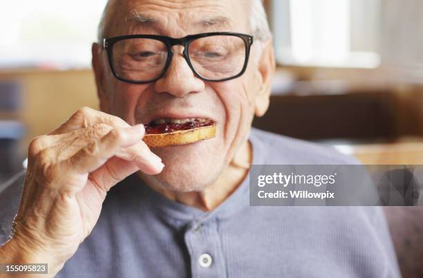 senior man eating toast and jelly jam - senior adult eating stock pictures, royalty-free photos & images