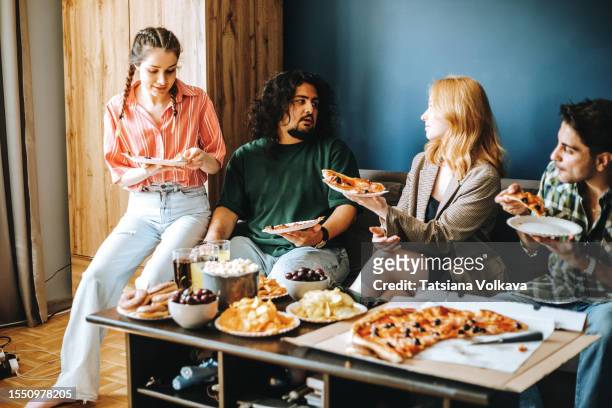photo of diverse group of college friends sitting on couch with array of delicious snacks eating pizza - pizza temptation stock pictures, royalty-free photos & images