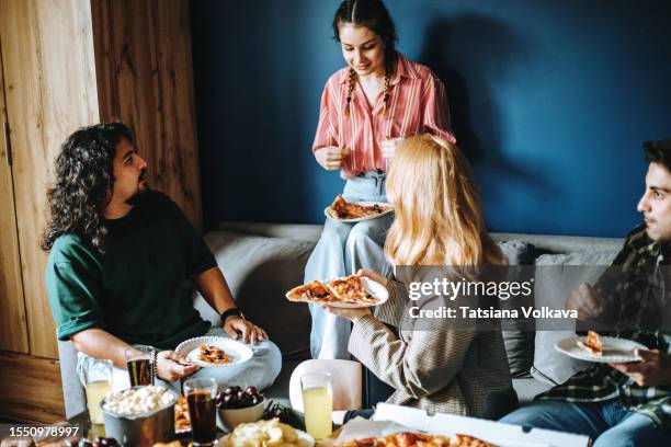 dynamic mix of friends gather around table with tempting snacks holding pizza slices - pizza temptation stock pictures, royalty-free photos & images