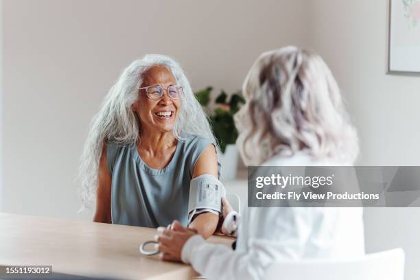 senior patient smiles as doctor takes her blood pressure - pacific islanders stock pictures, royalty-free photos & images