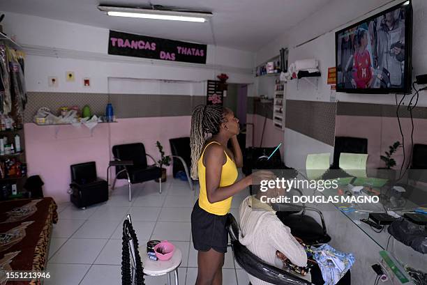 Brazilian football player, coach, and hairdresser Thatá Santos combs the hair of a client while watching the Australia and New Zealand 2023 Women's...