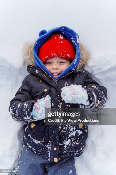 young girl smiles while laying in the snow - ski jacket stock pictures, royalty-free photos & images