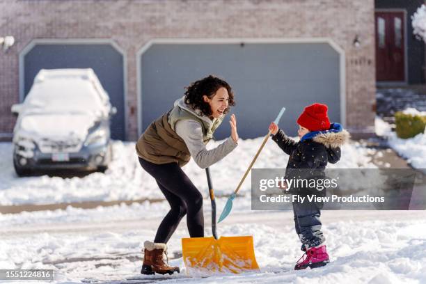 madre e hija chocan los cinco mientras la pala nieve - excavar fotografías e imágenes de stock
