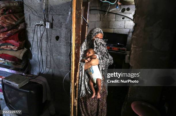 Palestinian mother wipes her face as she holds her baby during a heat wave and power outage in the Nuseirat refugee camp in the Gaza Strip on July...