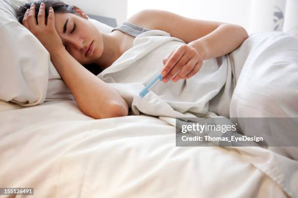 woman checking her temperature in bed - koorts stockfoto's en -beelden