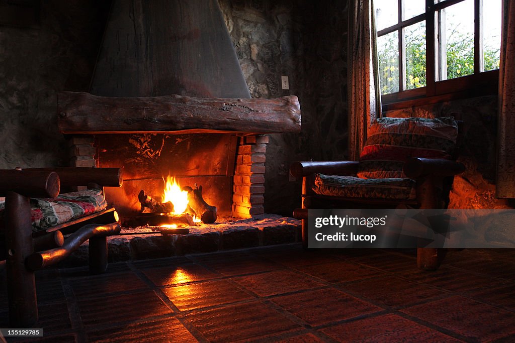 Fireplace with wooden logs, chairs and window