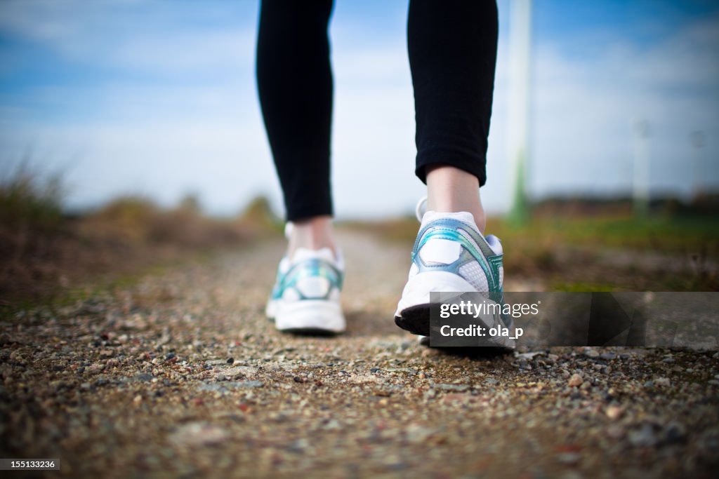 Woman's legs in black tights and white running shoes on dirt