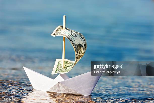 paper boat with $1 bill sail is blown onshore - sinking stockfoto's en -beelden