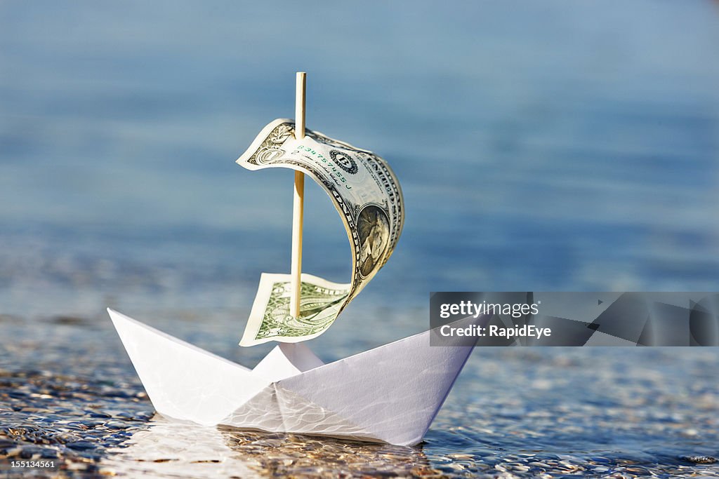 Paper boat with $1 bill sail is blown onshore