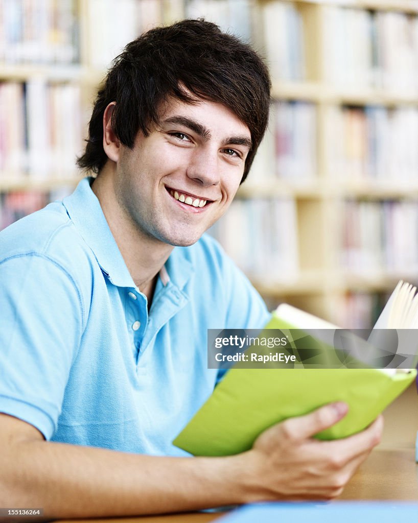 Handsome male student in library looks up from book smiling