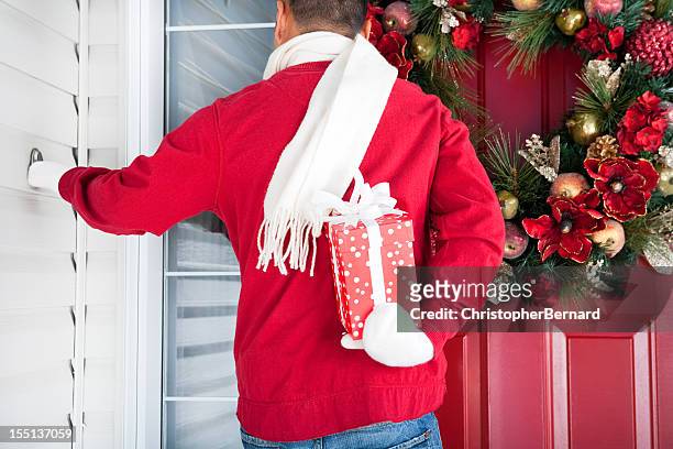smiling asian man holding christmas gift at front door - hiding behind back stock pictures, royalty-free photos & images