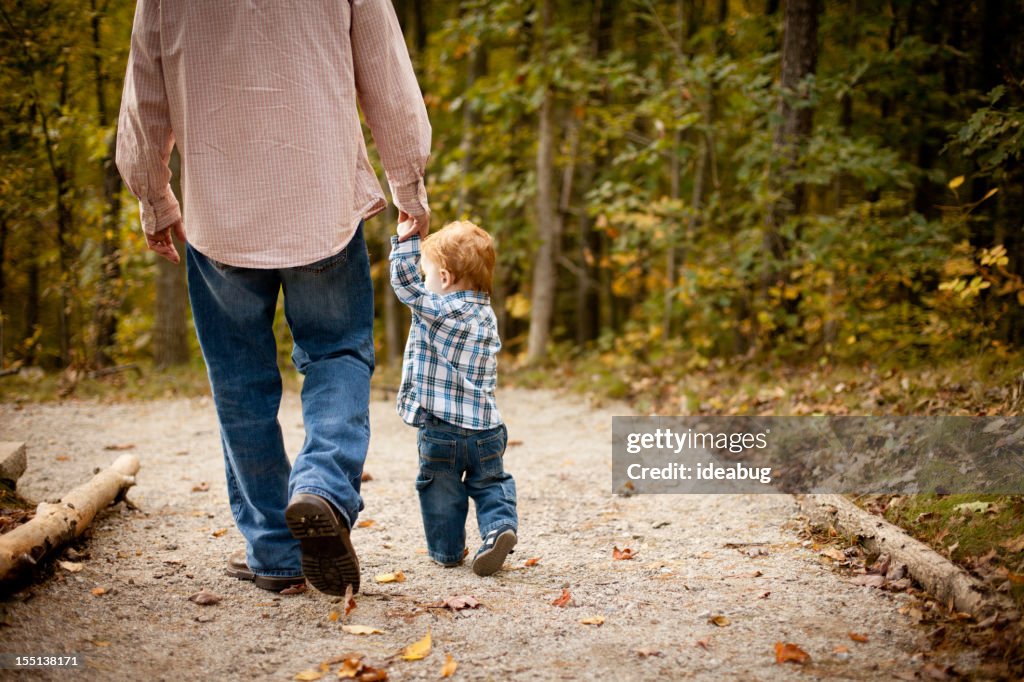 Father and Son Holding Hands While Walking through Autumn Woods