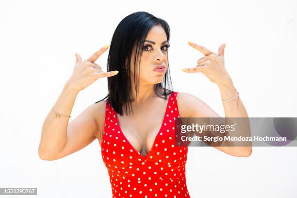 latino woman in a red polka dot dress looking at the camera and doing the heavy metal horns hand sign - heavy metal horns stock pictures, royalty-free photos & images