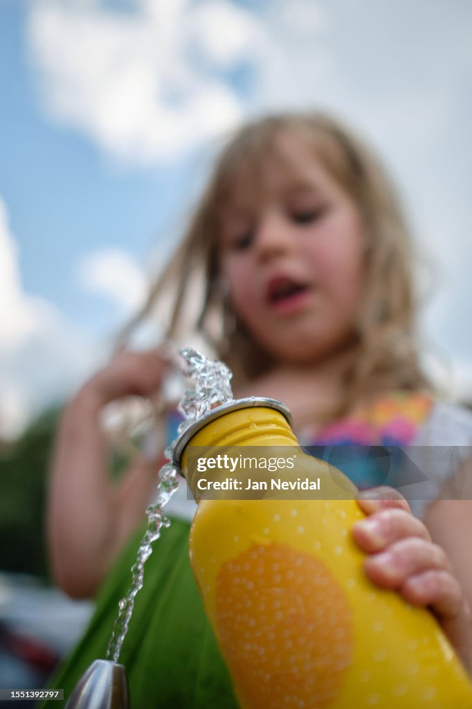 Small girl filling up metal yellow water bottle at public water fountain