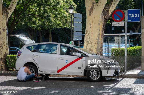 Taxi with a damaged tire due to a puncture is repaired by its driver at a taxi rank.