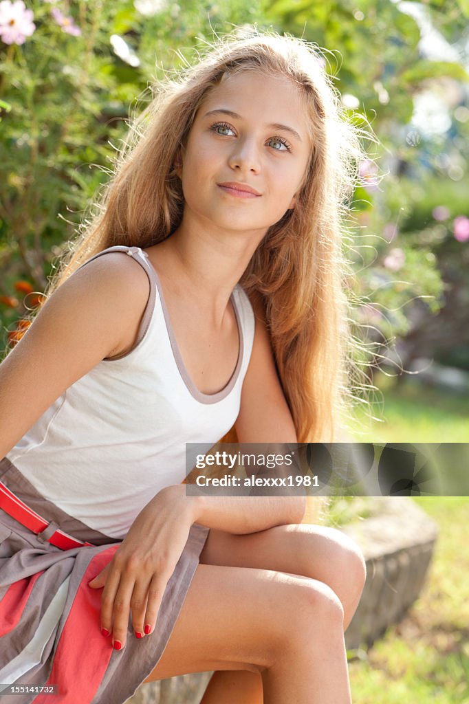 Beautiful female teenager sitting outdoors on curbs, posing, looking away