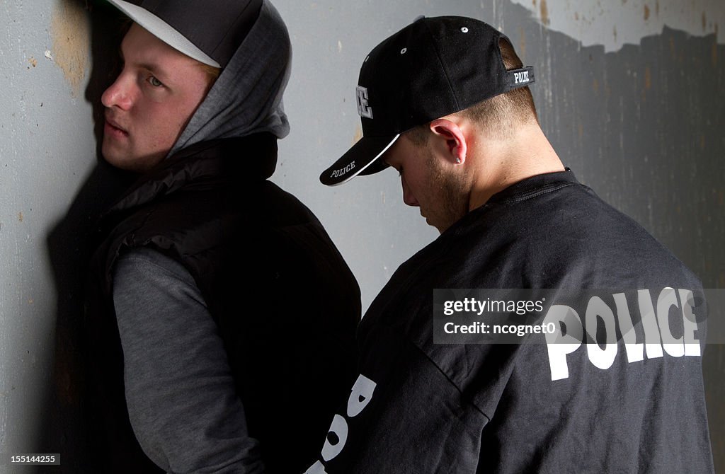 Man being handcuffed by a policeman against a gray wall