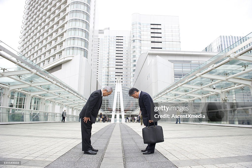 Two businessman bowing to each other on a pedestrian bridge