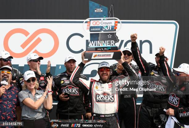 Martin Truex Jr., driver of the Reser's Fine Foods Toyota, lifts the Crayon 301 trophy in celebration in victory lane after winning the NASCAR Cup...
