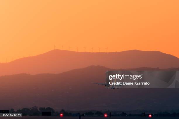 golden takeoff towards a sustainable future, airplane soaring at sunset with mountains and renewable energy wind turbines in the background - launch stock pictures, royalty-free photos & images