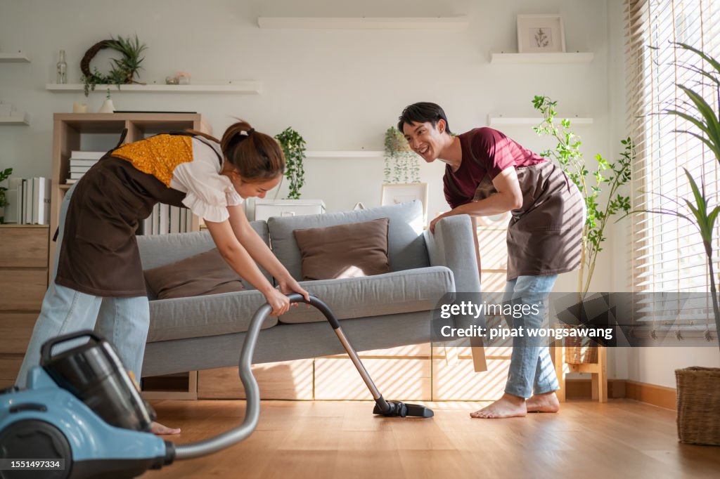 Asian young couple moving into a new house helping to clean the house by vacuuming, family relations concept, real estate