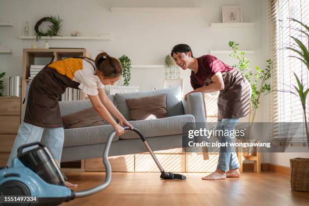 asian young couple moving into a new house helping to clean the house by vacuuming, family relations concept, real estate - aufräumen stock-fotos und bilder