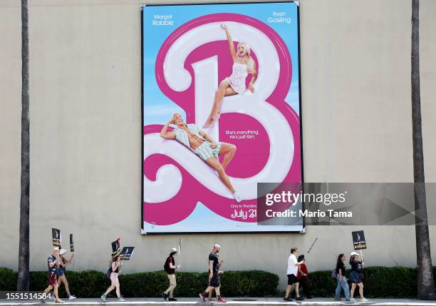 Striking SAG-AFTRA members picket with striking WGA workers on Day 5 near a billboard for the Barbie movie outside Warner Bros. Studio on July 17,...