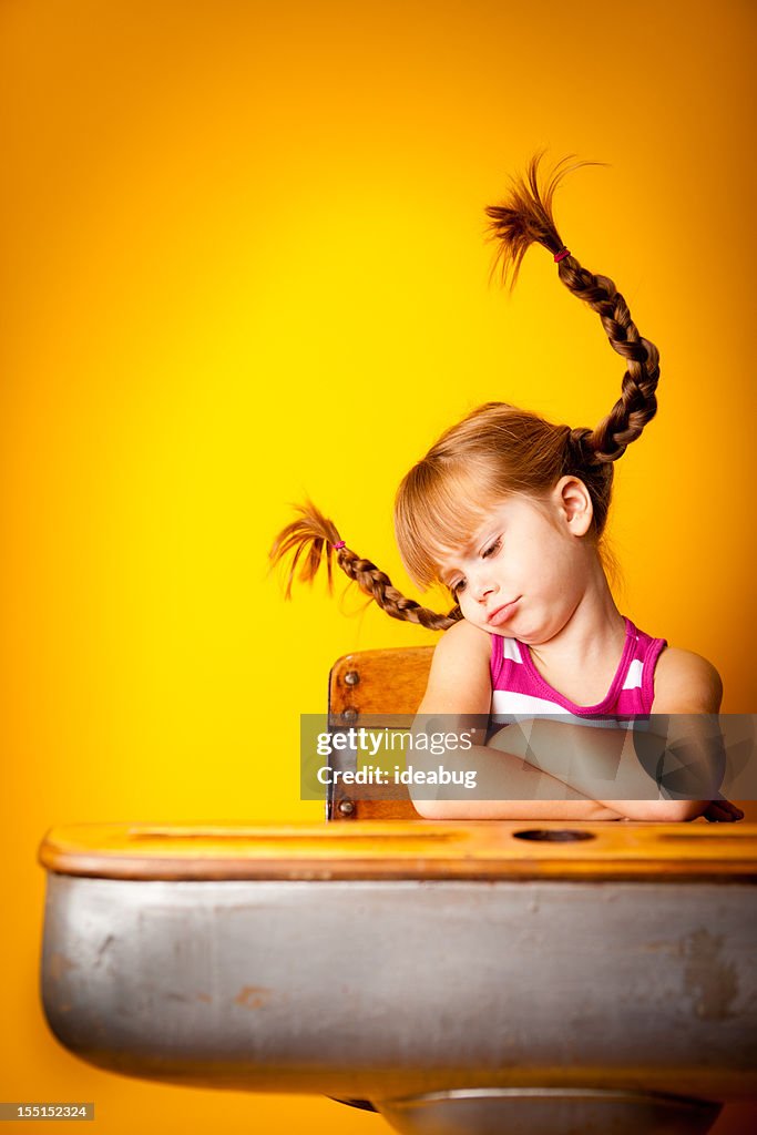 Frustrated, Red-Haired Girl with Upward Braids Sitting at School Desk