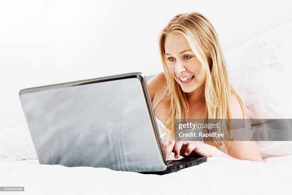 Bonita rubia mujer sonrisas como s'utiliza una computadora portátil en la cama