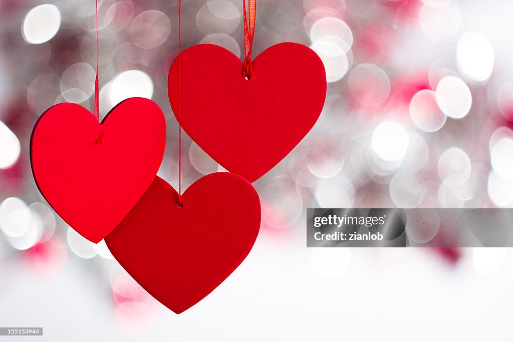 Three hanging red hearts on defocused light background.