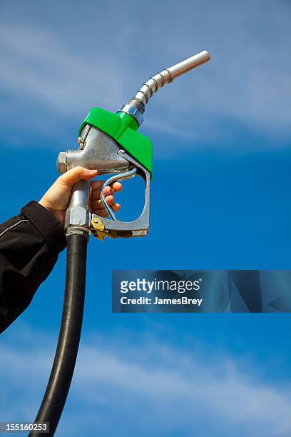 in gas we trust; gasoline pump nozzle held toward sky - industrial hose stockfoto's en -beelden