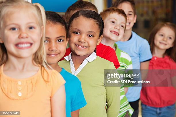 young elementary students smiling while waiting in line - kids in a row stock pictures, royalty-free photos & images