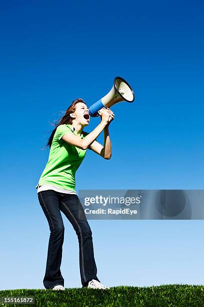 passionate young woman in field yells into bullhorn - protestor megaphone stock pictures, royalty-free photos & images