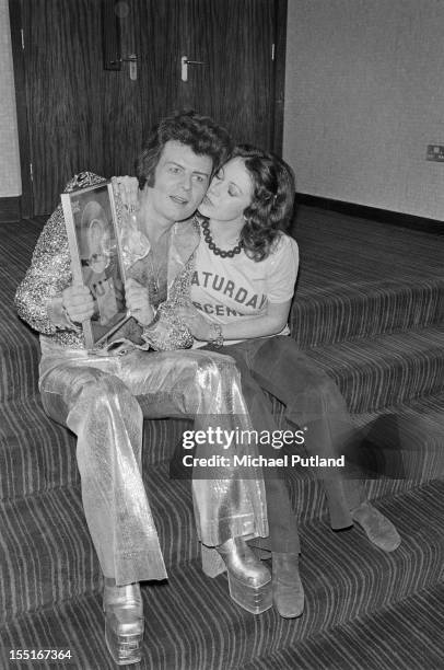 English pop singer Gary Glitter receives a kiss from a fan, 12th March 1974. He is holding an award for sales of his single 'I Love, You Love, Me...