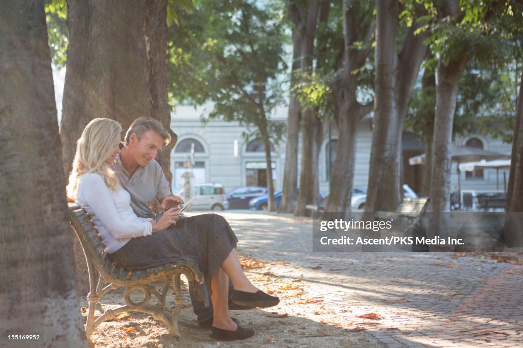 Couple use digital tablet from bench in park