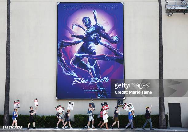 Striking SAG-AFTRA members picket with striking WGA workers on Day 5 near a billboard for the Blue Beetle movie outside Warner Bros. Studio on July...