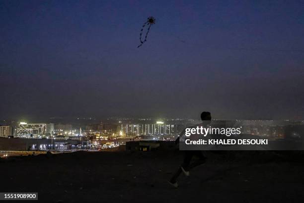 Kite flies in the air as a boy runs on a hill at the Moqattam district of Cairo as its skyline is lit up at dusk on July 24, 2023.