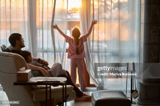 the girl opens the curtains of a large panoramic window and illuminates the room with warm sunset light. - house golden hour stock pictures, royalty-free photos & images