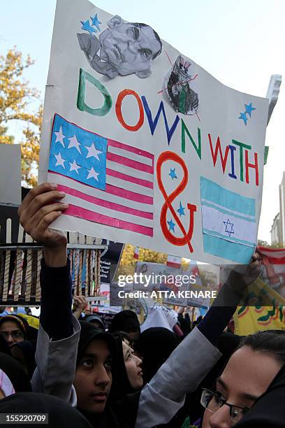 An Iranian woman holds an anti-US and Israeli slogan, bearing a crossed portrait of Uncle Sam, outside the former US embassy in Tehran on November 2...