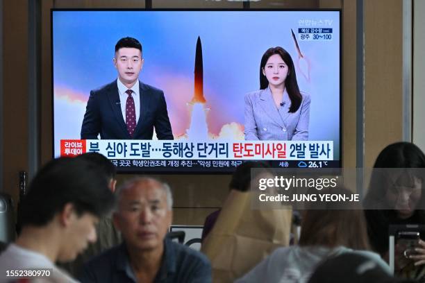 People watch a television screen showing a news broadcast with file footage of a North Korean missile test at a railway station in Seoul on July 25,...