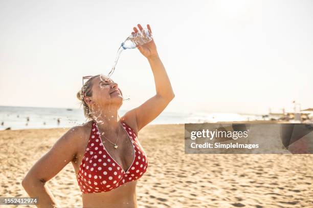 a young woman on the beach cools down with cold water during the summer heat. - ac weary stockfoto's en -beelden