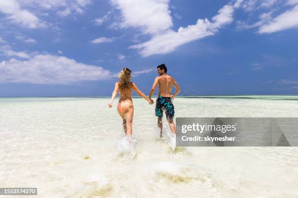 back view of carefree couple having fun while running through sea. - mid adult couple bildbanksfoton och bilder