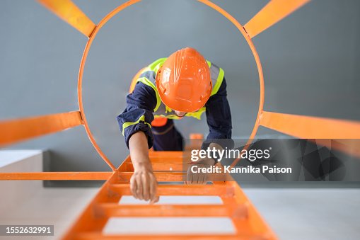 Blick aus hohem Winkel nach unten über die junge asiatische Technikerin, die auf die Leiter klettert, um die Maschine in einem Hochspannungstransformator-Umspannwerk zu inspizieren oder zu warten. Industrielles Gewerbe Beruf Arbeiter Konzept. Blick aus hohem Winkel nach unten über die junge asiatische Technikerin, die auf die Leiter klettert, um die Maschine in einem Hochspannungstransformator-Umspannwerk zu inspizieren oder zu warten. Industrielles Gewerbe Beruf Arbeiter Konzept.